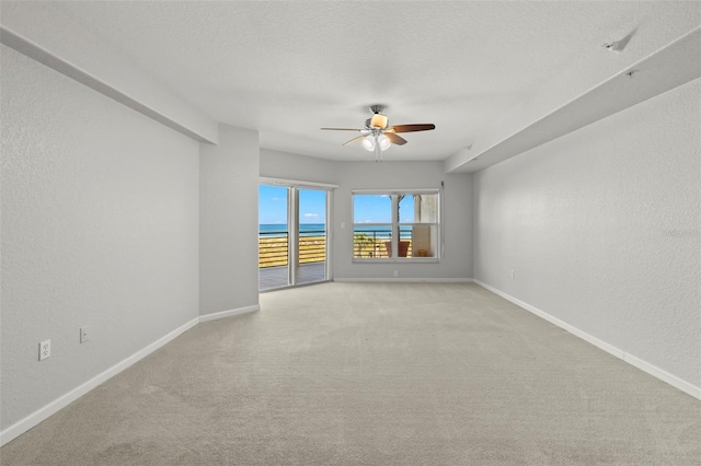 spare room with light carpet, a textured ceiling, ceiling fan, and a water view