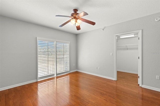 unfurnished bedroom with wood-type flooring, a walk in closet, a closet, and ceiling fan