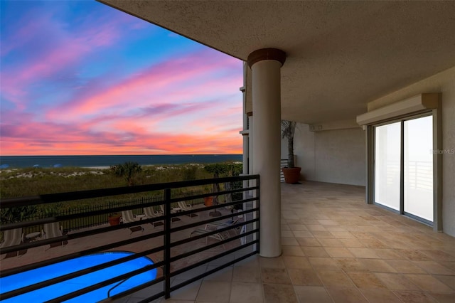 balcony at dusk featuring a water view