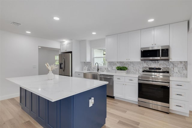 kitchen featuring white cabinetry, sink, a center island, light stone counters, and stainless steel appliances