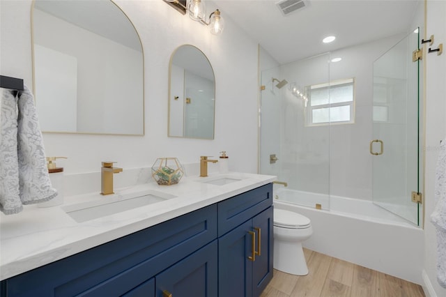 full bathroom with hardwood / wood-style flooring, vanity, combined bath / shower with glass door, and toilet