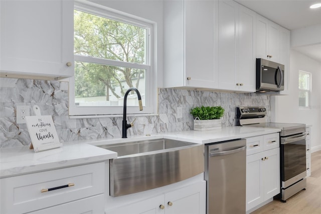 kitchen with sink, white cabinetry, stainless steel appliances, light stone counters, and decorative backsplash