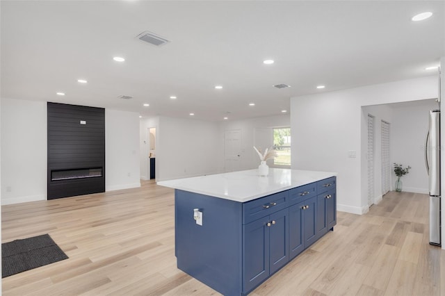 kitchen featuring blue cabinets, stainless steel refrigerator, a kitchen island, a fireplace, and light hardwood / wood-style floors