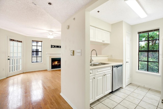 kitchen with light tile flooring, stainless steel dishwasher, white cabinets, sink, and a textured ceiling