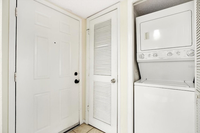 laundry room with light tile flooring, a textured ceiling, and stacked washer and dryer