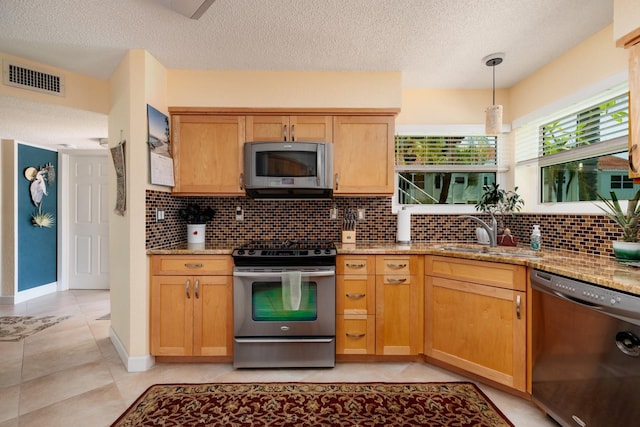 kitchen featuring stainless steel appliances, light stone counters, sink, and light tile floors