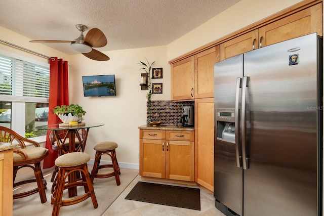 kitchen featuring light stone countertops, stainless steel refrigerator with ice dispenser, tasteful backsplash, light tile flooring, and ceiling fan