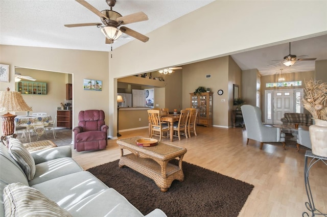 living room with ceiling fan, a textured ceiling, high vaulted ceiling, and light hardwood / wood-style flooring