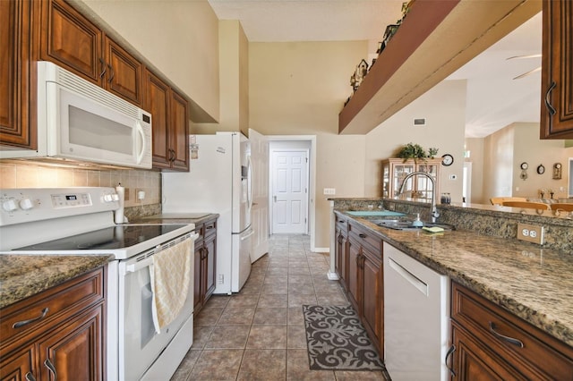 kitchen with white appliances, a high ceiling, sink, dark tile patterned floors, and stone countertops