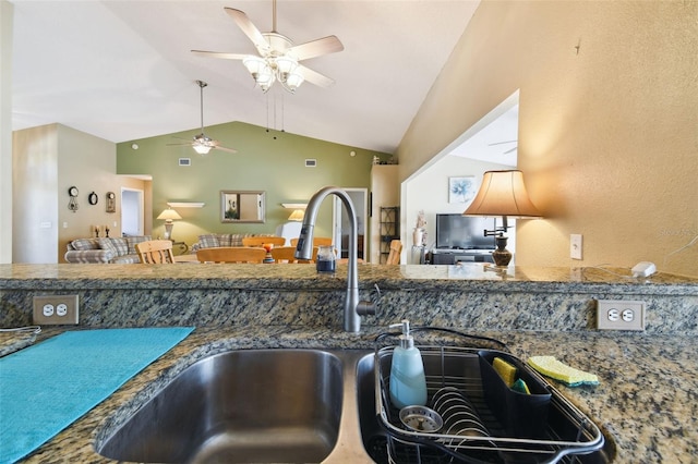 kitchen with ceiling fan, sink, dark stone counters, and vaulted ceiling