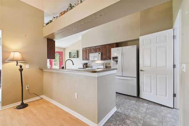 kitchen with kitchen peninsula, white appliances, a textured ceiling, light tile patterned floors, and lofted ceiling