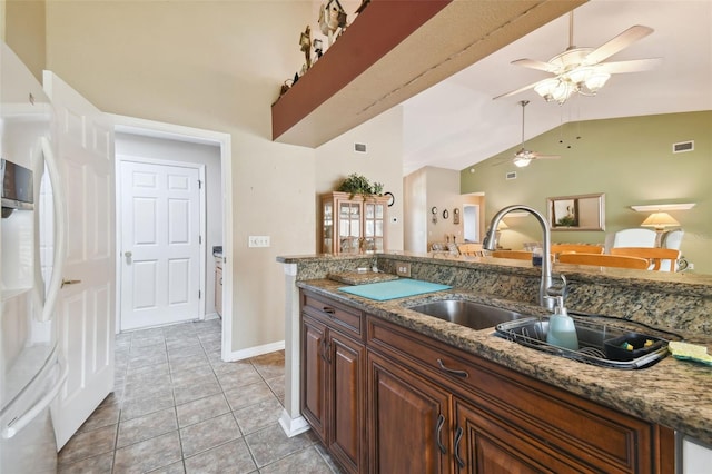 kitchen with tile patterned floors, dark stone countertops, white refrigerator with ice dispenser, and vaulted ceiling