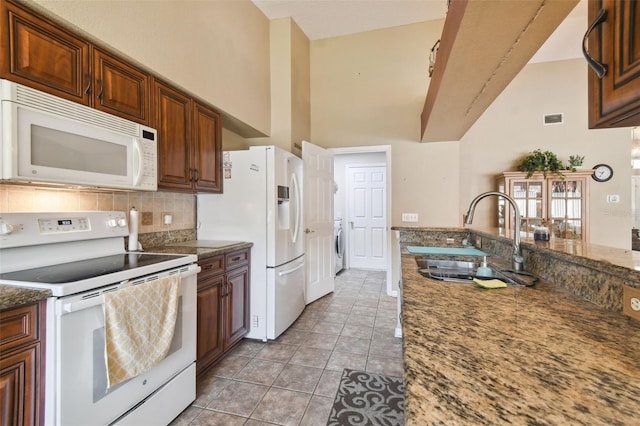 kitchen with white appliances, sink, light tile patterned floors, dark stone countertops, and washer / dryer