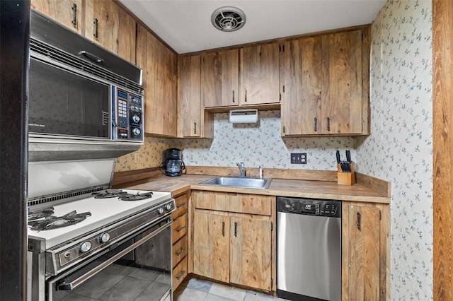 kitchen featuring stainless steel dishwasher, white gas stove, light tile patterned floors, and sink