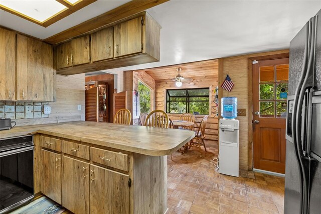 kitchen with wood walls, ceiling fan, stainless steel fridge, and kitchen peninsula