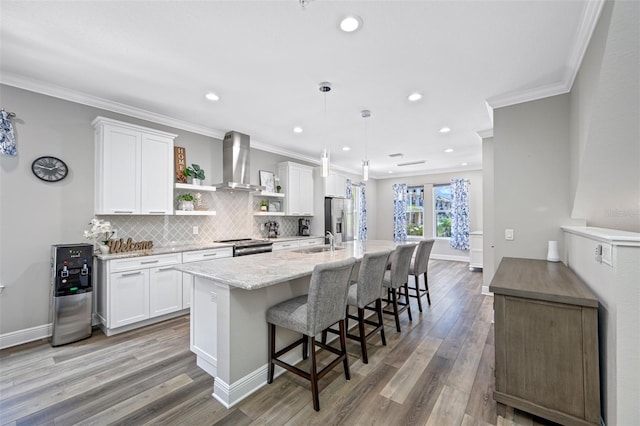 kitchen with wall chimney exhaust hood, appliances with stainless steel finishes, pendant lighting, white cabinets, and ornamental molding