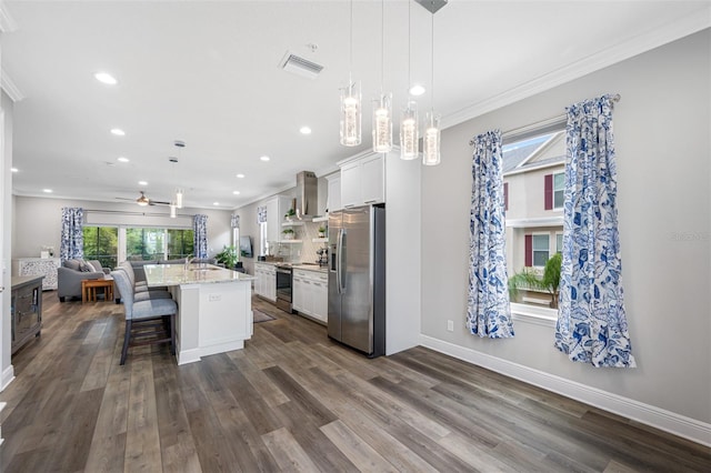 kitchen with white cabinets, decorative light fixtures, wall chimney range hood, and stainless steel appliances