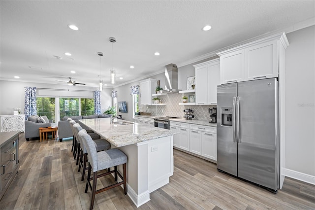 kitchen with white cabinets, appliances with stainless steel finishes, hanging light fixtures, and wall chimney exhaust hood