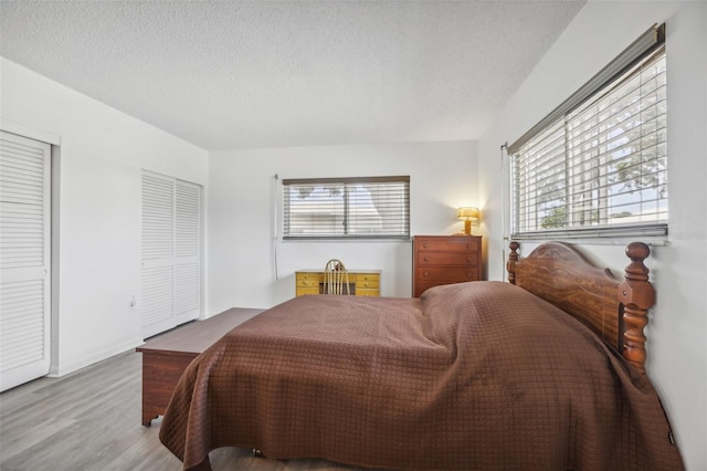 bedroom featuring two closets, light wood-type flooring, and a textured ceiling