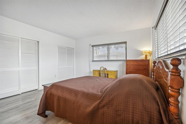 bedroom with a textured ceiling, two closets, and light hardwood / wood-style flooring