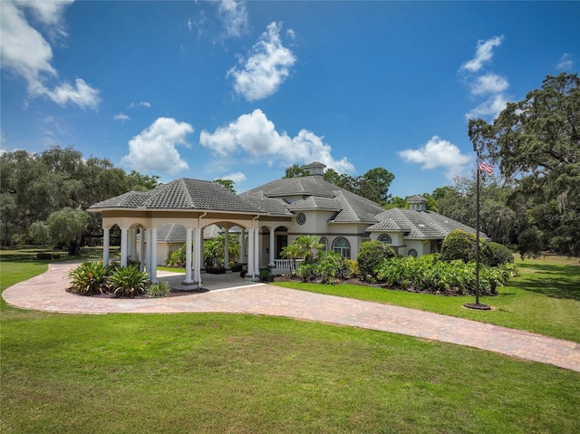 view of front of house featuring decorative driveway, stucco siding, a gazebo, a front yard, and a tiled roof