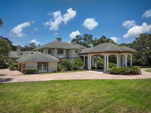 back of house with decorative driveway, a tile roof, a chimney, a lawn, and a gazebo