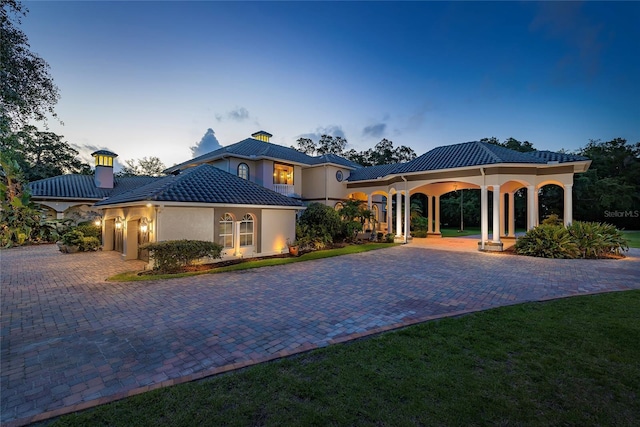 mediterranean / spanish house featuring a garage, a tiled roof, driveway, stucco siding, and a chimney