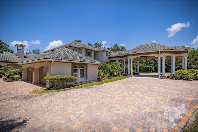 view of front of house featuring decorative driveway, a chimney, a tile roof, and stucco siding