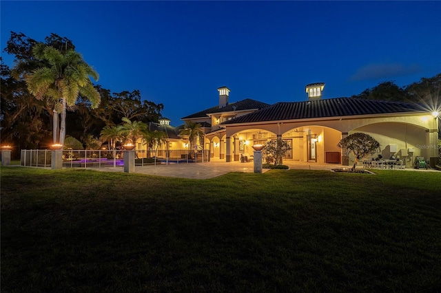 back of house at night featuring a patio area, fence, a lawn, and stucco siding