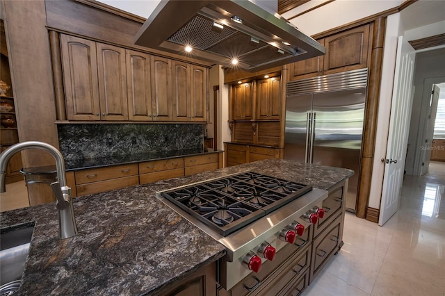 kitchen with wall chimney exhaust hood, dark stone countertops, backsplash, and stainless steel appliances