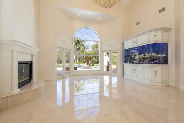 unfurnished living room featuring a glass covered fireplace, french doors, visible vents, and a high ceiling