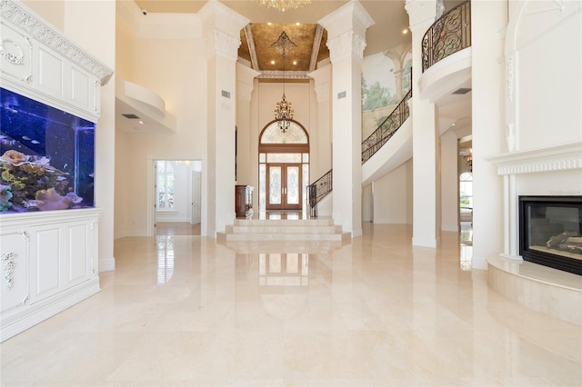 foyer with a notable chandelier, a towering ceiling, stairs, a glass covered fireplace, and crown molding