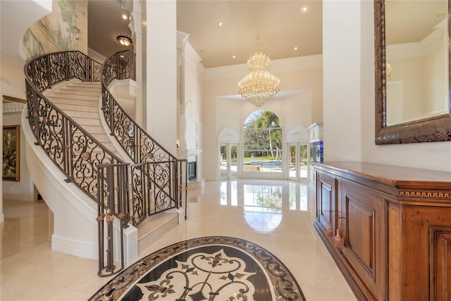 foyer entrance with baseboards, ornamental molding, marble finish floor, a high ceiling, and a chandelier