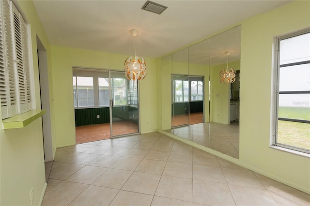 spare room featuring light tile patterned floors, a wealth of natural light, and an inviting chandelier