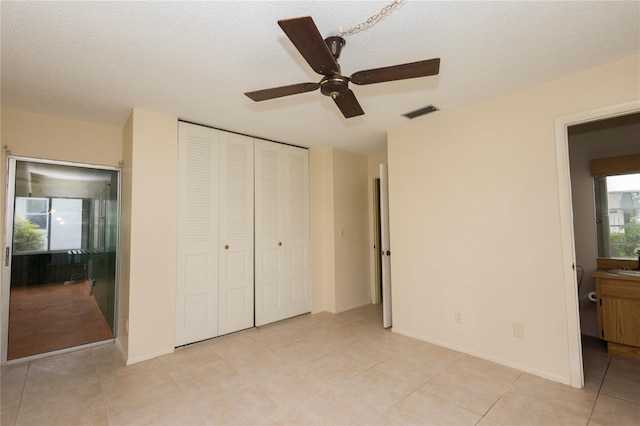 unfurnished bedroom with a textured ceiling, ceiling fan, light tile patterned floors, connected bathroom, and a closet