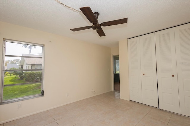 unfurnished bedroom with light tile patterned flooring, a textured ceiling, a closet, and ceiling fan