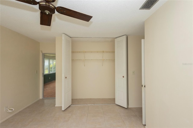 unfurnished bedroom featuring ceiling fan, a closet, a textured ceiling, and light tile patterned floors