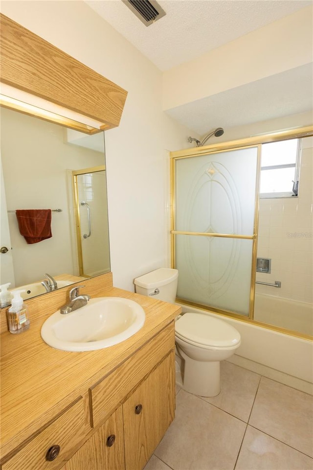 full bathroom featuring a textured ceiling, toilet, shower / bath combination with glass door, tile patterned flooring, and vanity