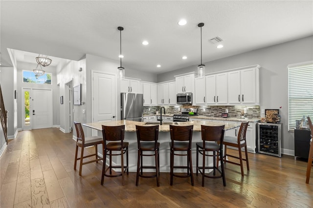 kitchen with dark hardwood / wood-style floors, hanging light fixtures, a center island with sink, wine cooler, and appliances with stainless steel finishes