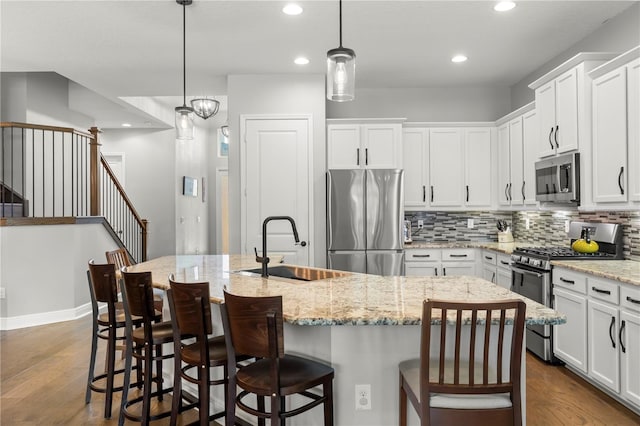 kitchen with stainless steel appliances, hardwood / wood-style floors, a center island with sink, and pendant lighting