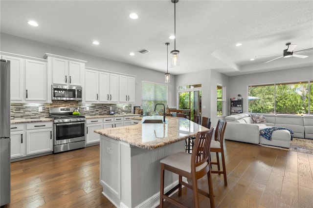 kitchen featuring dark hardwood / wood-style flooring, backsplash, hanging light fixtures, a kitchen island with sink, and appliances with stainless steel finishes