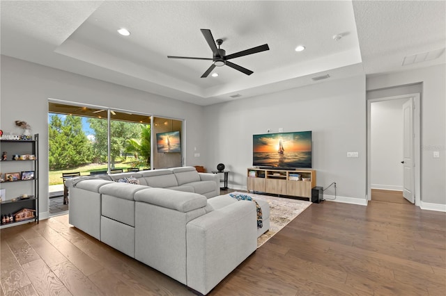 living room featuring hardwood / wood-style floors, ceiling fan, a tray ceiling, and a textured ceiling