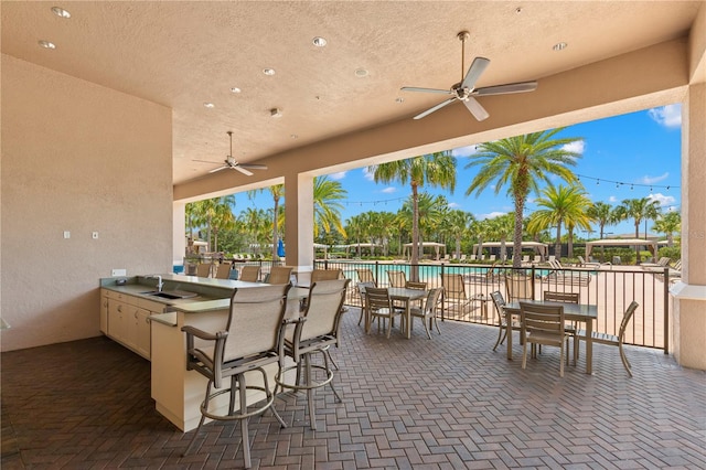 view of patio with a community pool, sink, and ceiling fan