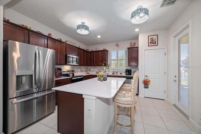 kitchen with a kitchen island, decorative backsplash, dark brown cabinets, stainless steel appliances, and light tile patterned floors