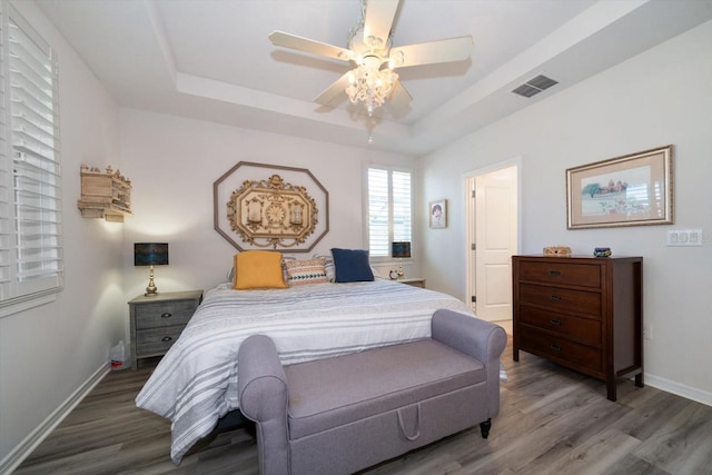 bedroom with a raised ceiling, wood-type flooring, and ceiling fan