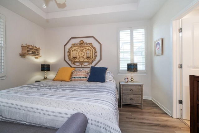 bedroom with ceiling fan, a raised ceiling, and hardwood / wood-style floors