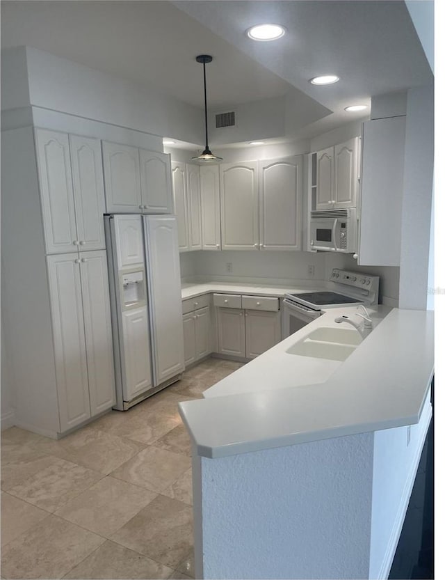 kitchen featuring light countertops, visible vents, a peninsula, white appliances, and hanging light fixtures