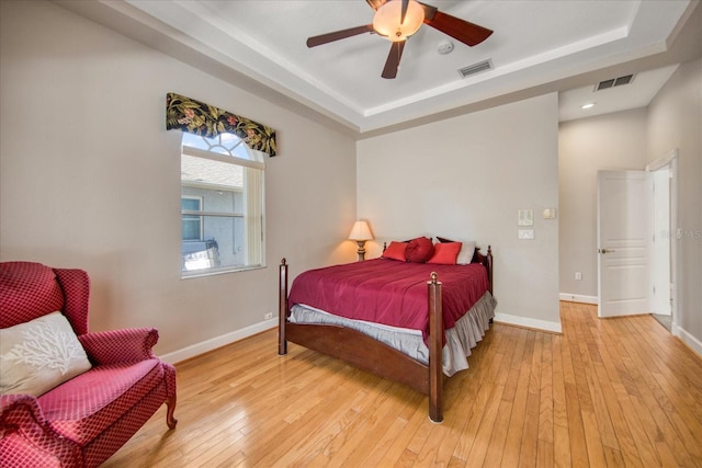 bedroom featuring ceiling fan, a tray ceiling, and light hardwood / wood-style flooring