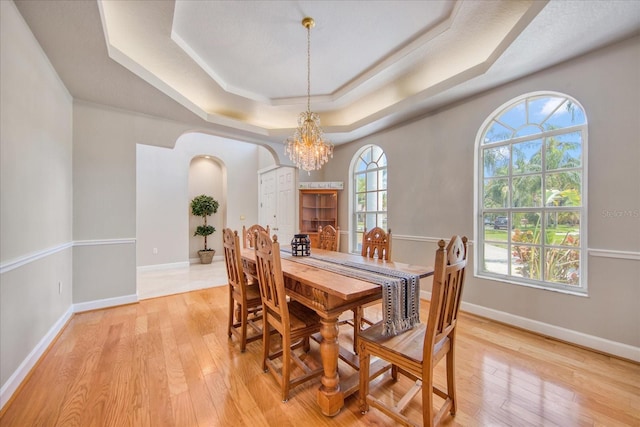 dining space featuring light wood-type flooring, an inviting chandelier, and a raised ceiling