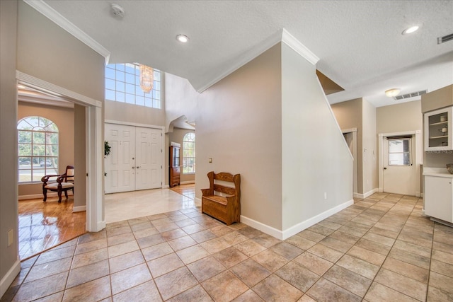 foyer with a wealth of natural light, crown molding, light tile patterned floors, and a textured ceiling